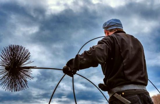 Sweep raising a flue brush against a coastal sky